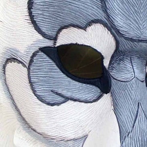Op de afbeelding: Close-up van een gebeeldhouwde uilsculptuur, met gedetailleerde veertjes in wit, grijs en zwart. Het oog van de uil is een donker, bladvormig ontwerp, dat diepte aan het kunstwerk toevoegt. Het oppervlak van de sculptuur heeft een getextureerd, gebeeldhouwd uiterlijk.