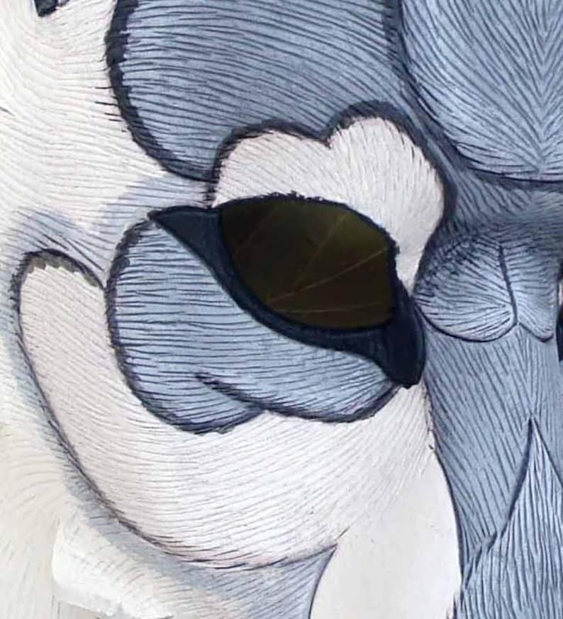 Op de afbeelding: Close-up van een gebeeldhouwde uilsculptuur, met gedetailleerde veertjes in wit, grijs en zwart. Het oog van de uil is een donker, bladvormig ontwerp, dat diepte aan het kunstwerk toevoegt. Het oppervlak van de sculptuur heeft een getextureerd, gebeeldhouwd uiterlijk.