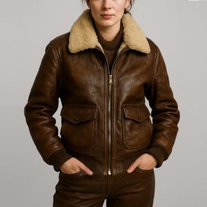 Puede incluir: Chaqueta bomber de cuero marrón con cuello de borrego beige. La chaqueta tiene dos bolsillos delanteros, dobladillo y puños de canalé y cremallera dorada. La modelo lleva un jersey y pantalones marrones. Estilo clásico.