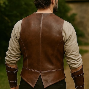 May include: A brown leather vest with a V-shaped hemline and a high back. The vest is worn over a long-sleeved, light-coloured shirt. Matching brown leather arm cuffs are visible. The person is standing outdoors.
