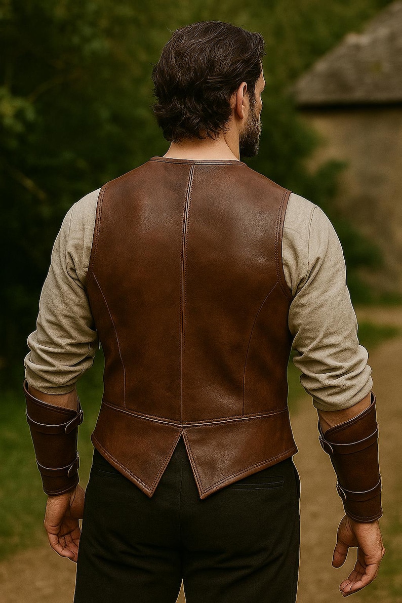 May include: A brown leather vest with a V-shaped hemline and a high back. The vest is worn over a long-sleeved, light-coloured shirt. Matching brown leather arm cuffs are visible. The person is standing outdoors.