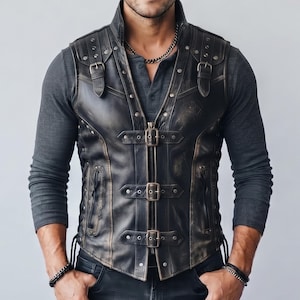 May include: A black leather waistcoat featuring a distressed finish, three front buckle closures, and two shoulder straps with buckles. The waistcoat includes silver-toned metal studs along the seams and vertical side lacing details, worn over a dark grey long-sleeve shirt.