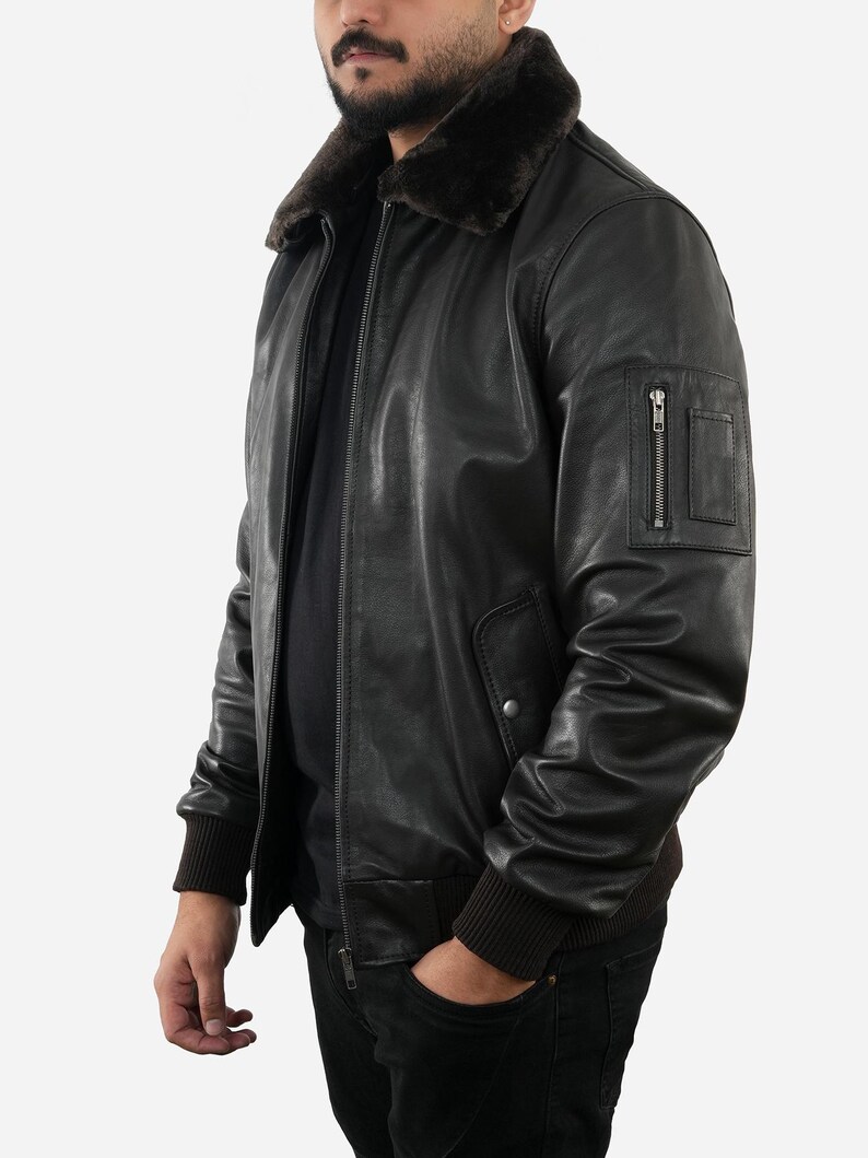 May include: A black leather bomber jacket with a brown fur collar. The jacket has a zipper closure, a small zippered pocket on the left sleeve, and ribbed cuffs and hem. The person is wearing black jeans.