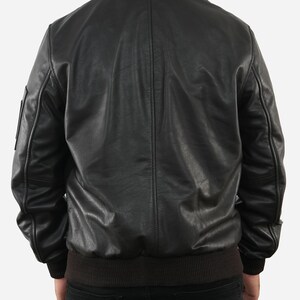 May include: Black leather bomber jacket with a brown faux fur collar and a ribbed hem. The jacket has a classic design with a smooth, matte finish. The back view shows the jacket's details, including the seams and the fit.