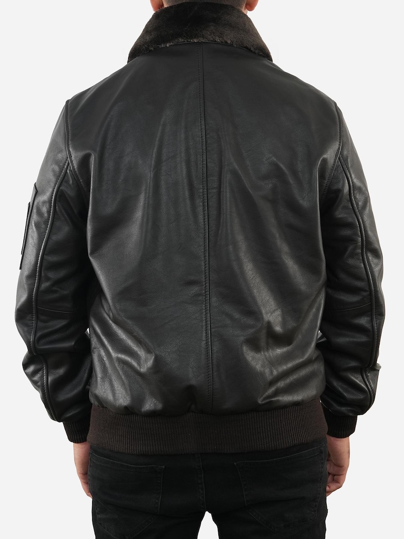 May include: Black leather bomber jacket with a brown faux fur collar and a ribbed hem. The jacket has a classic design with a smooth, matte finish. The back view shows the jacket's details, including the seams and the fit.