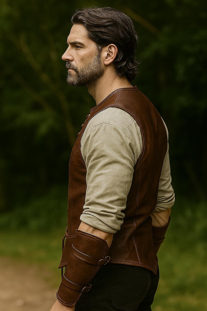 May include: A brown leather vest and matching arm guards are worn over a long-sleeved, light-coloured shirt. The vest has a classic design, and the arm guards are secured with buckles. The background is a blurred green, suggesting an outdoor setting.