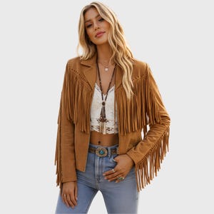 Puede incluir: Una chaqueta de ante color canela con largos flecos en el pecho, los hombros y las mangas. La chaqueta tiene cuello de solapa y se lleva sobre un top corto de encaje blanco y vaqueros azul claro con una hebilla de cinturón turquesa decorativa.