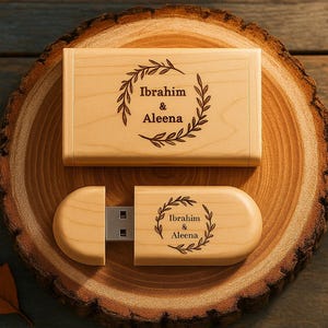 May include: A wooden USB flash drive and matching box, both engraved with the names "Ibrahim & Aleena" within a laurel wreath design. The items are displayed on a wooden slice, with a rustic aesthetic. The USB drive is open, revealing the metal connector.