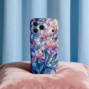 May include: A smartphone case featuring a stained-glass design of purple and pink iris flowers against a blue background. The case has a glossy finish and a protective design, with cutouts for the camera lenses.