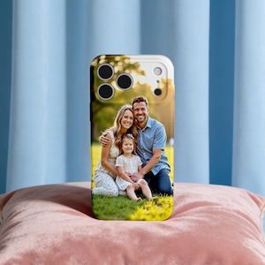 May include: A white and gold phone case featuring a family portrait. The image shows a smiling woman, man, and child sitting on the grass. The case has cutouts for the camera and buttons.