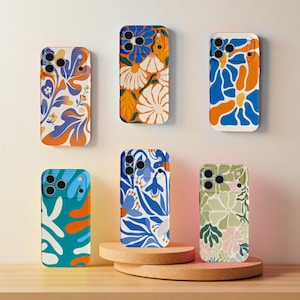 May include: A collection of six phone cases with floral designs. The cases feature colorful patterns in shades of blue, orange, white, and green. Some cases are displayed on a wooden stand.