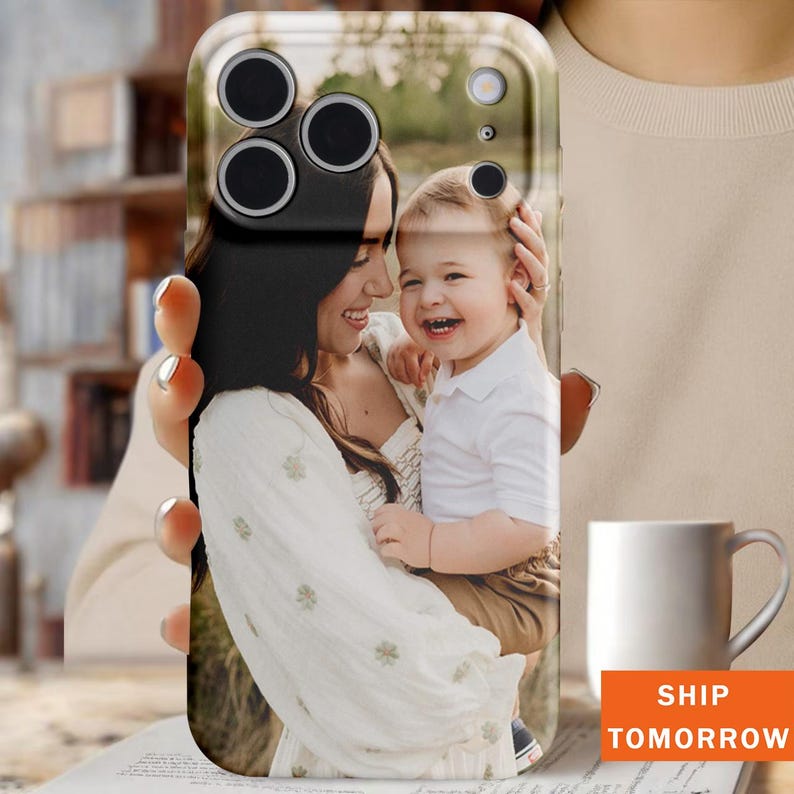 May include: A clear phone case featuring a photograph of a smiling woman and a child. The case has a black camera module and the text "SHIP TOMORROW" in an orange box.