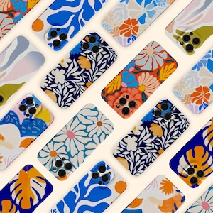 May include: A collection of colorful phone cases with floral and abstract designs. The cases feature various patterns, including daisies, leaves, and abstract shapes in shades of blue, orange, white, and yellow. The cases are arranged diagonally on a light beige background.