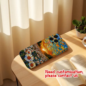 May include: A phone case with a vibrant mosaic design depicting a sunset and a field of daisies. The case has a blue camera module and the text "Need customization, please contact us". It rests on a wooden table.