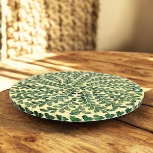 May include: Round green and white decorative tray with a leaf pattern. The tray is made of a natural material and has a rustic look.