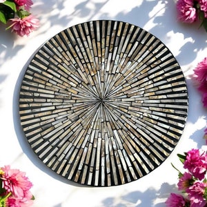 May include: A round, black tray with a sunburst design made of iridescent mother of pearl tiles. The tray is surrounded by pink flowers.