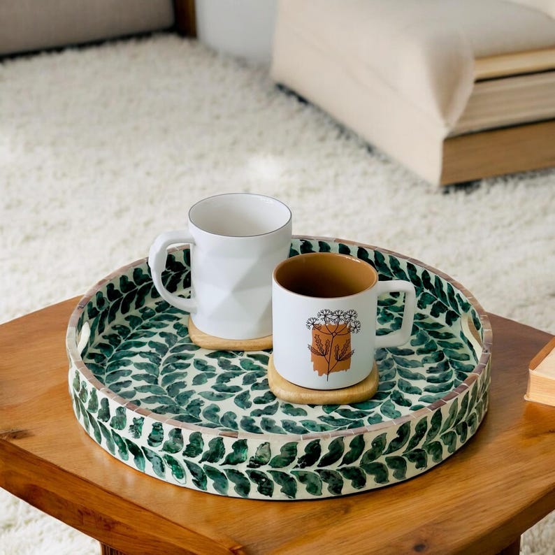 May include: A round serving tray with a green and white leaf design. Two white mugs with a floral design are on the tray.