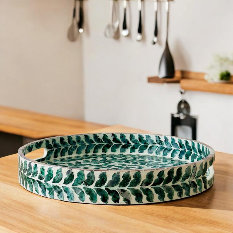 May include: A round serving tray with a white background and a green leaf design around the edge. The tray has two handles on the sides.