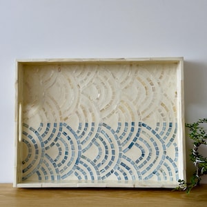 May include: A rectangular tray with a white and blue mosaic design. The top half of the tray is white with a subtle pattern of beige and white circles. The bottom half of the tray is blue with a pattern of blue and white circles.