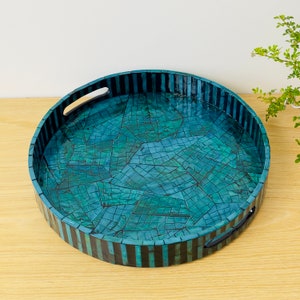 Puede incluir: Bandeja redonda para servir con un diseño de mosaico azul y negro. La bandeja tiene un borde rayado en blanco y negro y dos asas.