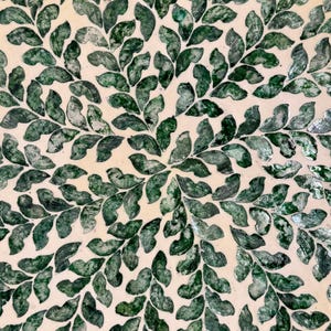 May include: A circular decorative tray with a white background and a pattern of green leaves made from mother of pearl.