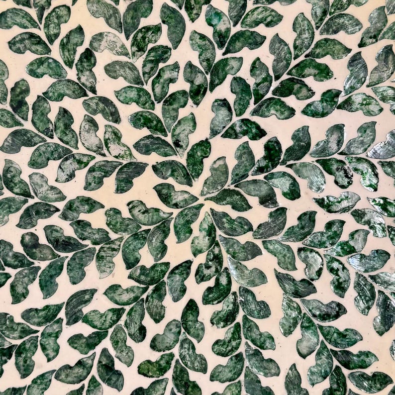 May include: A circular decorative tray with a white background and a pattern of green leaves made from mother of pearl.