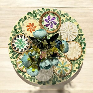 May include: A decorative plate with a green and white design featuring multiple circular patterns. The plate is decorated with a cluster of blue and green flowers in the center.