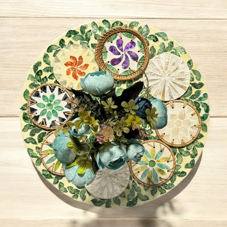May include: A decorative plate with a green and white design featuring multiple circular patterns. The plate is decorated with a cluster of blue and green flowers in the center.