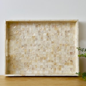 May include: A rectangular tray made of mother of pearl tiles in a white and cream colour. The tray has a wooden frame and two handles on the sides.