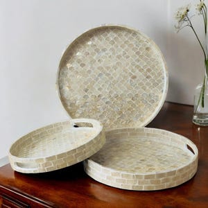 May include: Three round trays made of mother of pearl with a white and beige mosaic pattern. The largest tray has a scale pattern, while the two smaller trays have a brick pattern.