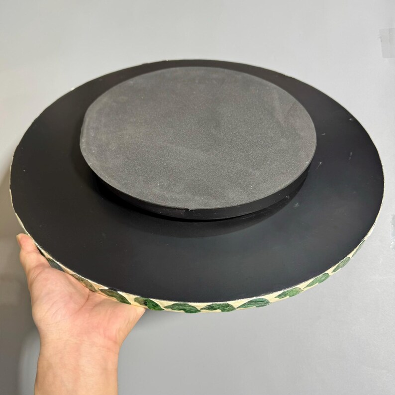 May include: A round, black, decorative tray with a green leaf pattern around the edge. The tray has a black foam base.