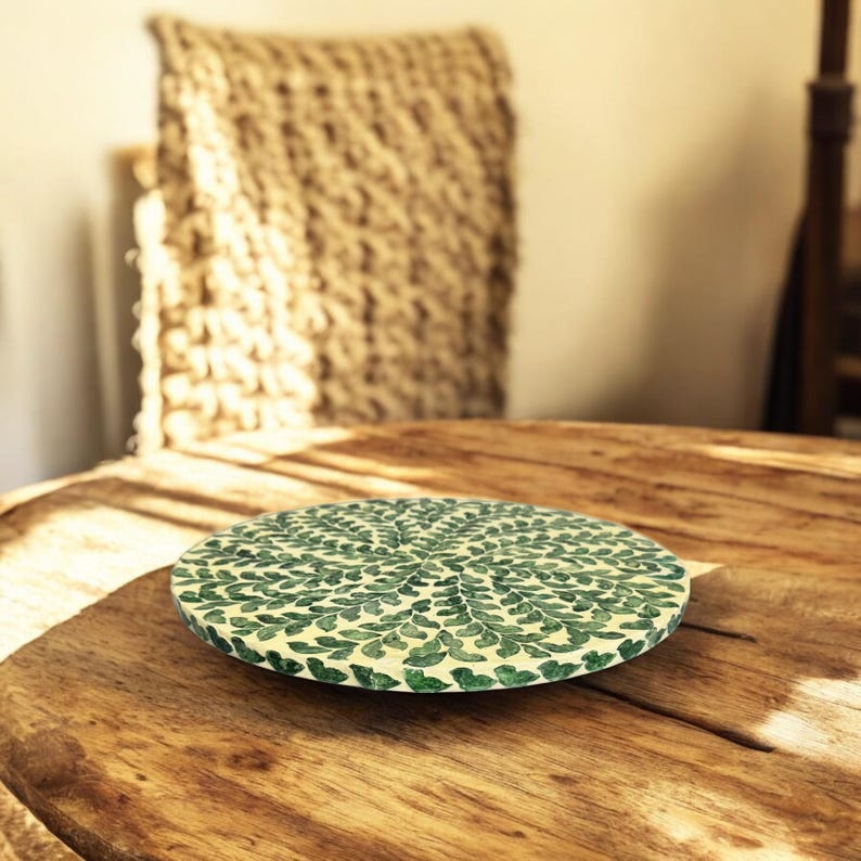 May include: Round green and white decorative tray with a leaf pattern. The tray is made of a natural material and has a rustic look.