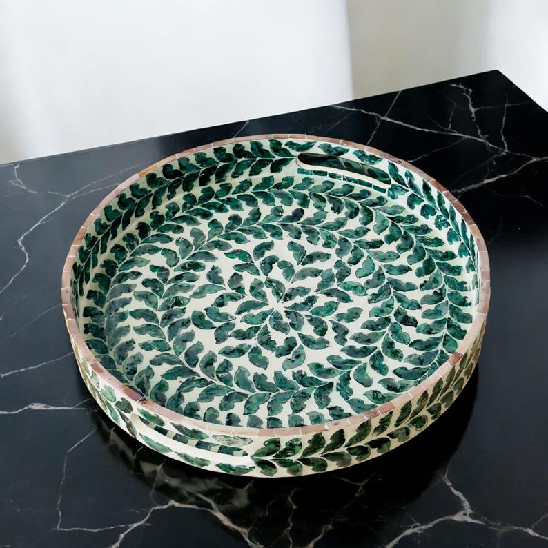 May include: A round tray with a white background and a green leaf pattern. The tray has a handle on the side.