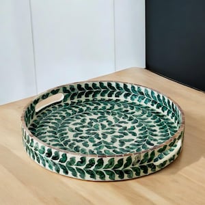 May include: Round serving tray with a green leaf design. The tray has a white background and a wooden handle.
