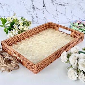 Op de afbeelding: Rechthoekig geweven rotan dienblad met een lichtgekleurd, mozaïekachtig oppervlak. De lade heeft ingebouwde handgrepen en is omgeven door een bruine rand. Decoratieve bloemen en touw liggen op de achtergrond.