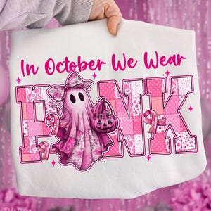 May include: White t-shirt with the text "In October We Wear PINK". The word PINK is in a patchwork design with pink ribbons. A pink ghost with a bow and a pumpkin bucket is in the center.