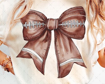 May include: A brown football-shaped bow with white stitching. The bow is tied in a knot and the ends are flowing down. The bow is on a white t-shirt.