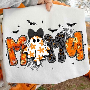 Op de afbeelding: Witte Halloween-afbeelding met het woord "MOM" en een spook en vleermuizen. De "M" is oranje met griezelige ontwerpen, de "O" is een spook met een zwarte strik en de tweede "M" is zwart met Halloween-patronen.