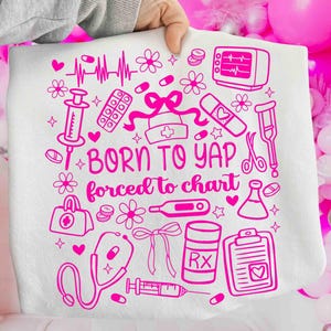May include: White throw blanket featuring a pink medical design. The design includes a stethoscope, pills, a syringe, a heart monitor, and the text "BORN TO YAP forced to chart."