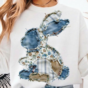 May include: White sweatshirt with a patchwork bunny design. The bunny is made from denim, floral, and striped fabrics. The design is centrally placed on the front of the long-sleeved top, offering a textured appearance. A casual, comfortable garment.