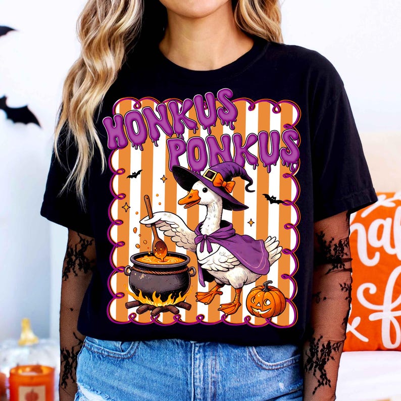 May include: Black t-shirt with a Halloween-themed graphic. The design features a goose wearing a witch hat and cape, stirring a cauldron. The text "HONKUS PONKUS" is above the goose. A pumpkin is also included in the design.