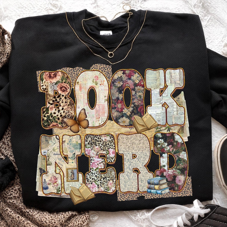 May include: Black sweatshirt with the words "BOOK NERD" in a large, decorative font. The letters are filled with floral, leopard print, and vintage paper patterns. A butterfly and small books are also featured.