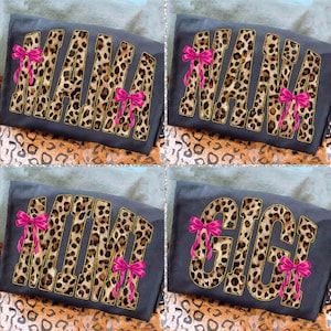 May include: Four dark gray t-shirts with leopard print lettering spelling "MAMA", "NANA", "MIMI", and "GIGI". Each shirt has a bright pink bow on the letters. The background has a leopard print pattern.