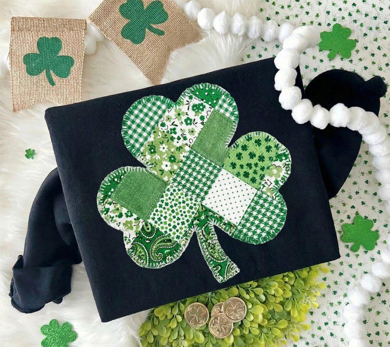 Puede incluir: Camiseta negra de manga larga con un gran dise&ntilde;o de tr&eacute;bol de retazos en varios tonos de verde y blanco. La camiseta est&aacute; decorada con un tr&eacute;bol y monedas de oro, perfecta para el D&iacute;a de San Patricio.