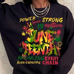 May include: Black sweatshirt featuring a vibrant Juneteenth design. The graphic includes the words "POWER," "STRONG," "June 19," "culture," "JUNE TEENTH," "BREAKING EVERY CHAIN," and "BLACK IS BEAUTIFUL."