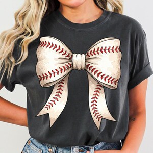 May include: A gray t-shirt with a white baseball-stitched bow on the front.