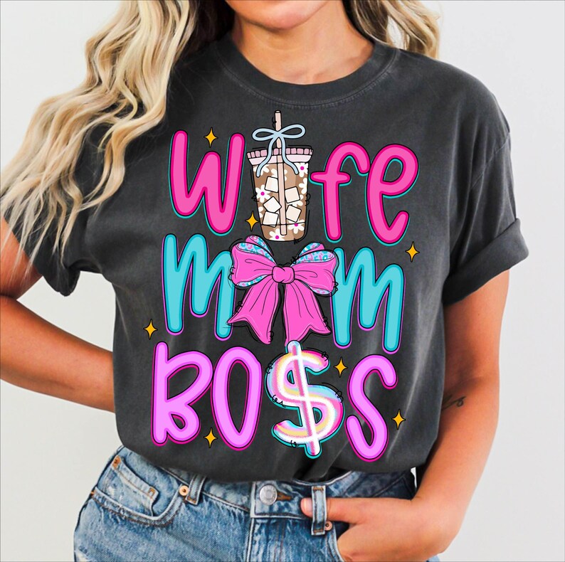 May include: Dark gray t-shirt with the words "Wife Mom Boss" in pink and turquoise lettering. A pink bow and a coffee drink graphic are also featured. The shirt is made of a soft material.