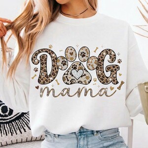 May include: White sweatshirt with the text "DOG mama" in a decorative font. The word "DOG" is in a leopard print design, with a paw print in the center. The design includes paw prints, hearts, and bones.