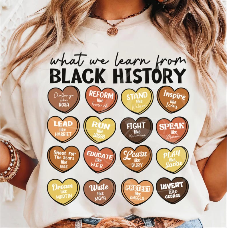 May include: Cream-colored t-shirt with the text "what we learn from BLACK HISTORY." The shirt features heart-shaped graphics with inspirational words and names like Rosa, Harriet, and Martin. A necklace and bracelets are also visible.
