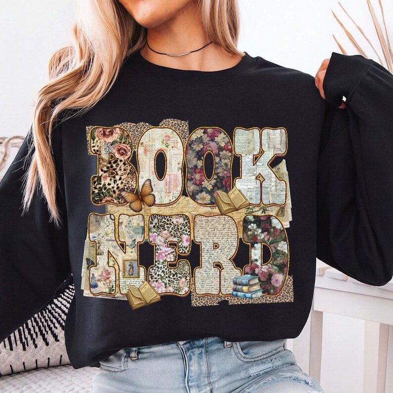 May include: Black sweatshirt with the words "BOOK NERD" in a collage of floral, leopard print, and book page patterns. A butterfly and small books are also featured in the design. The sweatshirt is a comfortable, casual style.